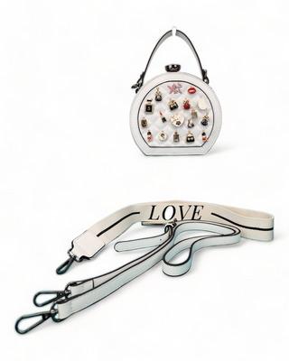 White crossbody handbag with a quilted face and adorned with charms and straps.
