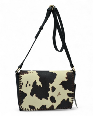 Cow print handbag with a black strap on a white background