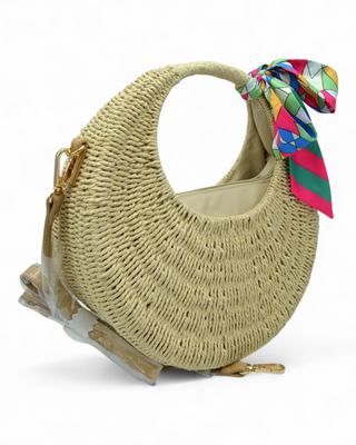 Round woven raffia handbag with a colorful scarf tied to the handle and detachable strap.