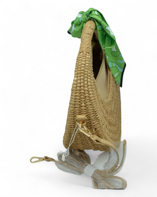 Round woven raffia handbag with a colorful scarf tied to the handle and detachable strap.