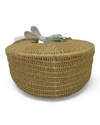 Round woven raffia handbag with a colorful scarf tied to the handle and detachable strap.