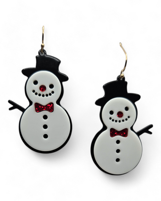 A pair of dangle earrings shaped like jolly snowmen, featuring black top hats, red glitter bow ties, and matching red noses. The snowmen have black arms and buttons, adding to their playful design.
