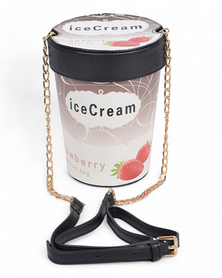 A novelty crossbody bag shaped like a strawberry ice cream pint, featuring a printed lid, strawberry details, and a gold chain strap with an additional black adjustable faux leather strap